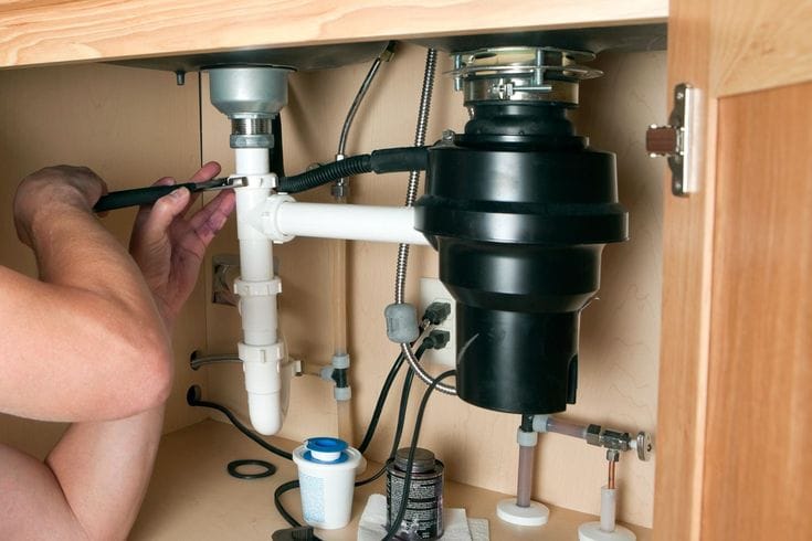 Plumber installing a garbage disposal beneath a kitchen sink in Denver