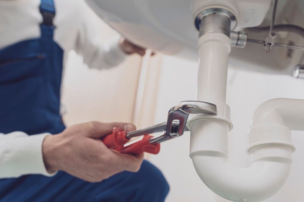 Plumber repairing a white drain pipe beneath a sink in Denver